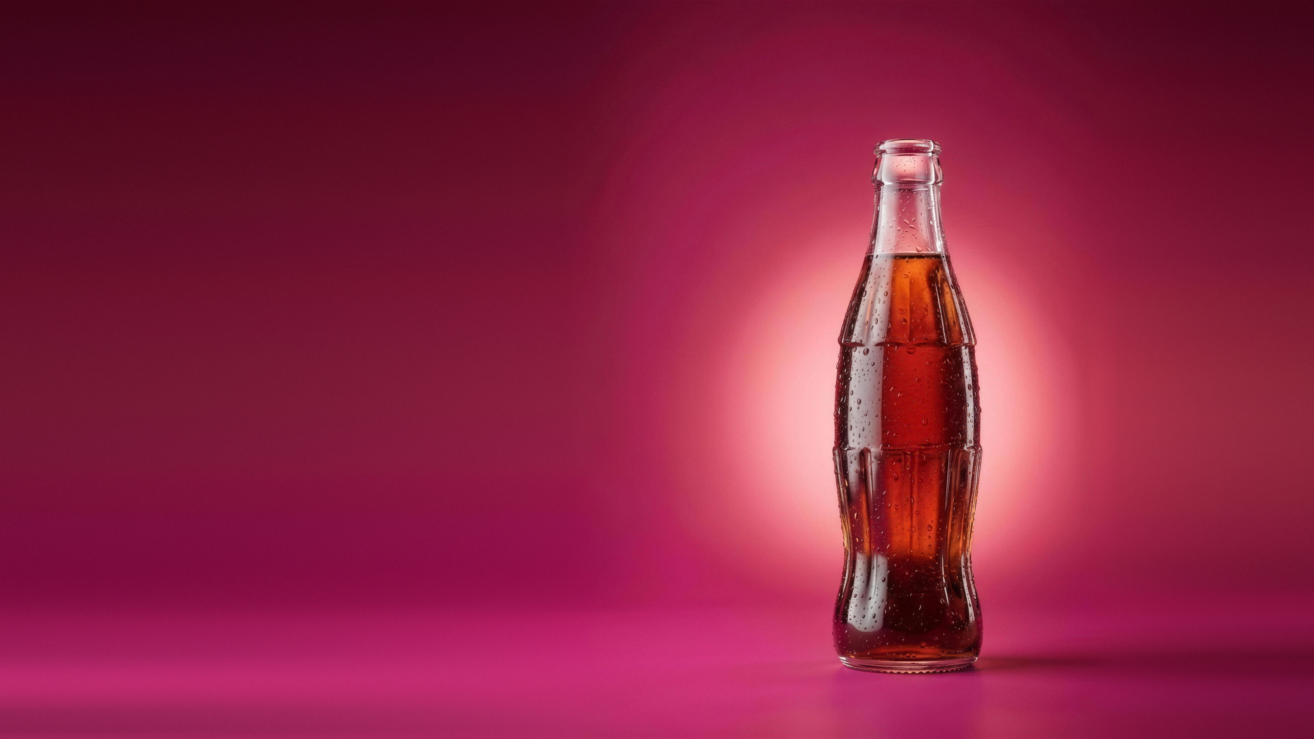 A chilled bottle of cola sweetened with TomorrowSweet™, lit against a deep crimson sweep