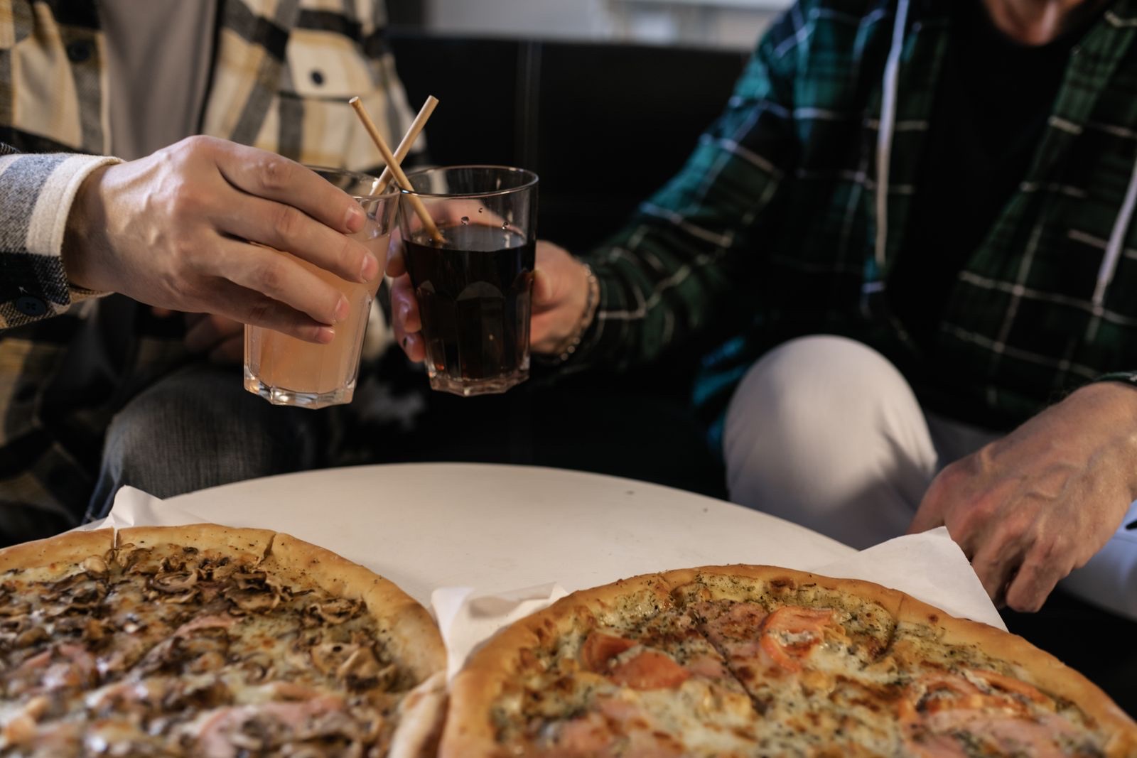 Friends toasting cold drinks together over pizza